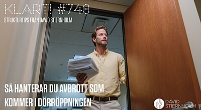 En man i en gul skjorta står i en dörröppning och håller en stor bunt papper i en kontorsmiljö.