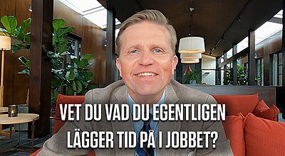 En leende man i kostym sitter i en modern loungemiljö med den svenska texten "Vet du vad du egentligen lägger tid på i jobbet?" visad i förgrunden.