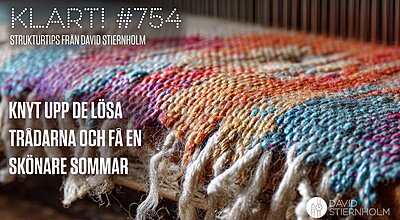 En färgglad vävd textil med fransar vilar på en träyta och uppvisar invecklade mönster i nyanser av blått, orange, rött, lila och cremevitt.