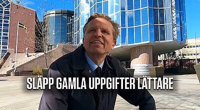 En leende man i en mörk jacka står utomhus framför moderna glasbyggnader med en svensk flagga synlig, med texten "SLÄPP GAMLA UPPGIFTER LÄTTARE" visad längst ned.