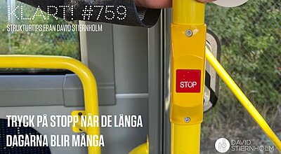 En hand håller i ett gult handtag på en buss, nära en röd "STOP"-knapp som används för att signalera till föraren att stanna vid nästa hållplats.