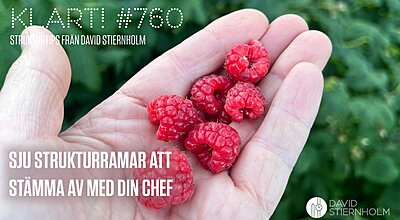 En hand håller flera färska röda hallon mot en suddig grön lövbakgrund.