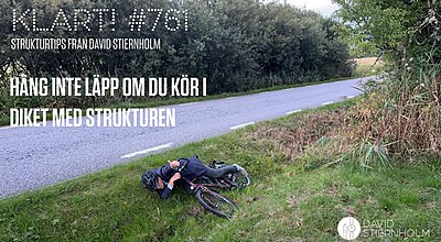 En cyklist ligger på en gräsbevuxen vägkant bredvid sin välta cykel och ger tummen upp.