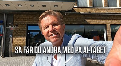 En leende man i en ljusblå kavaj tar en selfie utanför en tegelbyggnad, med den svenska texten "SÅ FÅR DU ANDRA MED PÅ AI-TÅGET" överlagd på bilden.