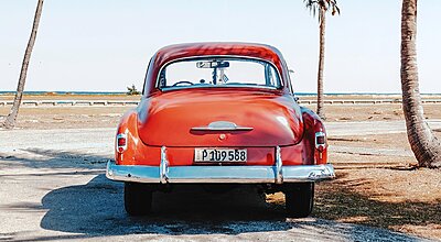 An old orange car on a beach with palms