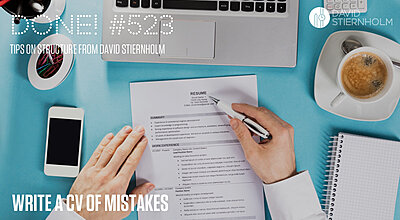 Two shirt dressed hands skimming through a CV on a blue desk, pen in hand.