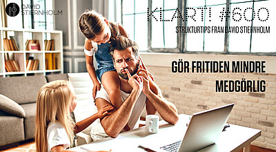 En man i skägg sitter vid ett skrivbord i hemmiljö med en dotter på axlarna och en dotter bredvid samtidigt som han försöker sköta ett jobbsamtal i telefon.