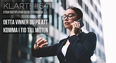 Ung affärskvinna i svart kavaj talar i telefon utomhus och tittar på sin klocka. Snart börjar mötet.